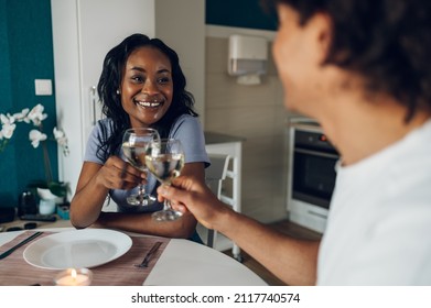 Beautiful African American Couple Having Romantic Dinner Together In Kitchen At Home. Millennial Couple's Lifestyle. Toasting With Wine Glasses.