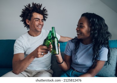 Beautiful African American Couple In Love Enjoying Their Free Time And Sitting On A Couch While Drinking Beer And Chatting At Home. Casual Date At Home.