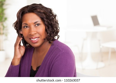 Beautiful African American Female Executive With Dark Brown Hair At Work In An Office Setting Wearing A Purple Sweater.