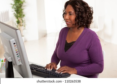 Beautiful African American Female Executive With Dark Brown Hair At Work In An Office Setting Wearing A Purple Sweater.