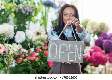 beautiful african american florist holding open sign and smiling at camera - Powered by Shutterstock