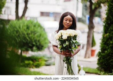 Beautiful african american girl holding bouquet of white roses flowers on dating in the city. Black businesswoman with bunch of flowers.