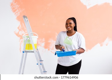 Beautiful African American Girl Painting The Wall With Paint Roller. Portrait Of A Young Beautiful Woman Painting Wall In Her New Apartment. Redecoration And Renovation Concept.