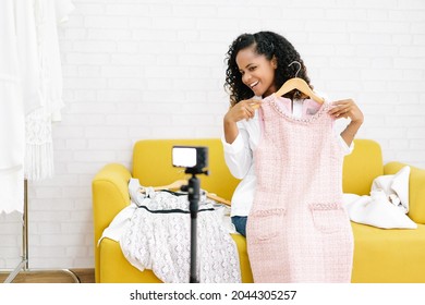 Beautiful african american girl vlogger or blogger sitting on sofa and live streaming for sale fashion clothing on social network. Her is influencer in social online. Social media marketing concept.