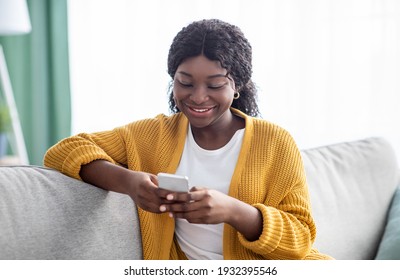 Beautiful African American Lady With Smartphone Enjoying Weekend At Home, Closeup Portrait. Smiling Young Black Woman Chatting With Friends Or Lover, Using Mobile Phone, Living Room Interior