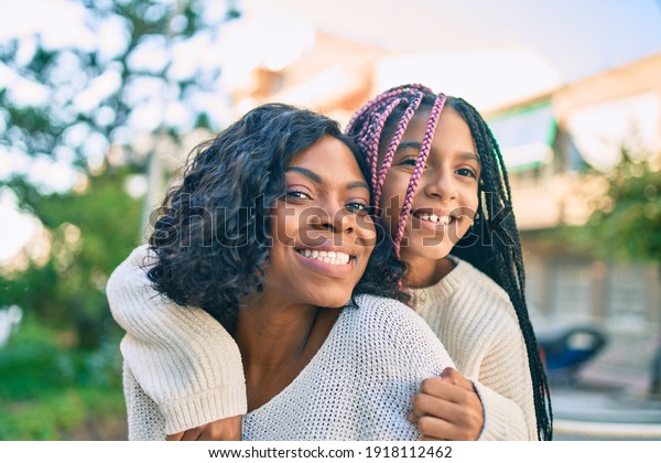 Beautiful african american mother\
giving daughter piggyback ride smiling happy at the\
park.