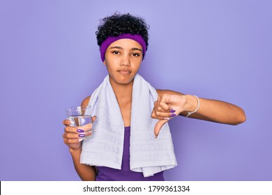 Beautiful African American Sporty Woman Doing Exercise Wearing Towel Drinking Glass Of Water With Angry Face, Negative Sign Showing Dislike With Thumbs Down, Rejection Concept