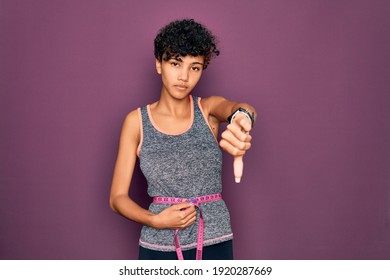 Beautiful African American Sporty Woman Doing Exercise Controlling Weight Using Tape Measure With Angry Face, Negative Sign Showing Dislike With Thumbs Down, Rejection Concept