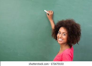 Beautiful African American student or teacher standing in front of the blank class blackboard with a piece of chalk in her hand ready to commence writing - Powered by Shutterstock