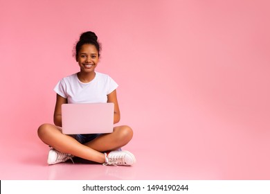 Beautiful African American Teen Sitting With Laptop In Lotus Position On Pink Studio Background