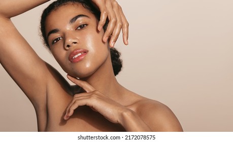 Beautiful african american woman, 25 years old, has glowing skin, nourished face after cream, skincare gel or moisturizer, posing against brown background