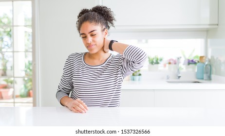Beautiful african american woman with afro hair wearing casual striped sweater Suffering of neck ache injury, touching neck with hand, muscular pain