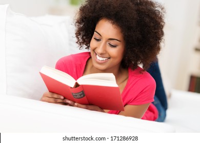 Beautiful African American woman with an afro hairstyle sitting reading a book with a smile of pleasure