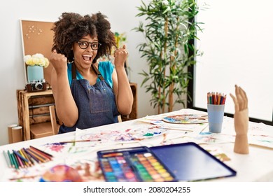 Beautiful african american woman with afro hair painting at art studio celebrating surprised and amazed for success with arms raised and open eyes. winner concept.  - Shutterstock ID 2080204255