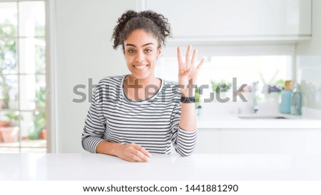 Beautiful african american woman with afro hair wearing casual striped sweater showing and pointing up with fingers number four while smiling confident and happy.