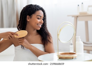 Beautiful African American Woman Combing Her Curly Hair With Bamboo Brush At Home While Sitting Near Mirror In Bathroom, Young Black Lady Looking At Her Reflection And Smiling, Closeup Shot - Powered by Shutterstock