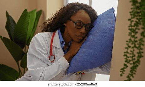 A beautiful african american woman doctor with curly hair wearing a white coat and glasses, resting on a cushion in a hospital waiting room. - Powered by Shutterstock