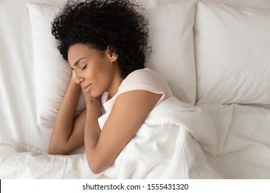 Beautiful African American woman with hands under cheek sleeping in bed under blanket top view, girl with closed eyes resting in bedroom, enjoying fresh bedclothes, lying on soft pillow close up - Powered by Shutterstock