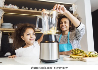 Beautiful African American woman and her daughter making a smoothie in the kitchen 