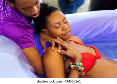 A beautiful African American woman labors peacefully in a birthing tub as her husband comforts her by holding her hand and rubbing her back.