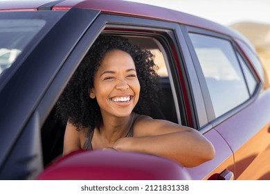 Beautiful African American Woman Looking Outside Car During Summer Holiday. Young Attractive Black Woman Laughing And Enjoying Road Trip On A Summer Day. Happy Girl Driving A Red Car With Big Grin.