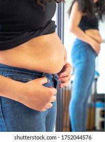 Beautiful African American Woman And Mother Stands In Front Of A Mirror And Attempts To Try To Close Her Tight Fitting Blue Jeans Pants After Postpartum Diet And Weight Loss Exercise.