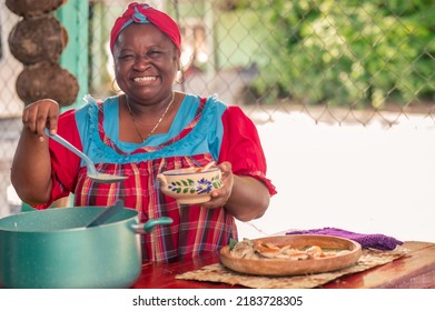 A Beautiful African American Woman On The Patio Of Her House Serving Soup. A Senior Adult Woman Smiling And Looking At The Camera As She Serves A Plate Of Food. 