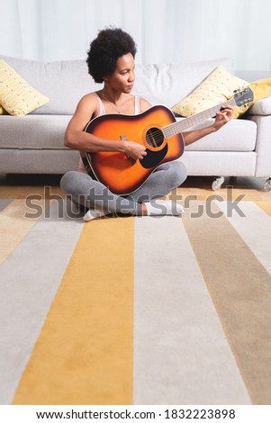 Beautiful african american woman playing guitar sitting on carpet at home