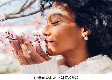 Beautiful African American woman smelling the soft, fresh and natural scent of pink flowers in spring in bloom. Concept of softness, delicacy, purity, femininity, dream of relaxation.