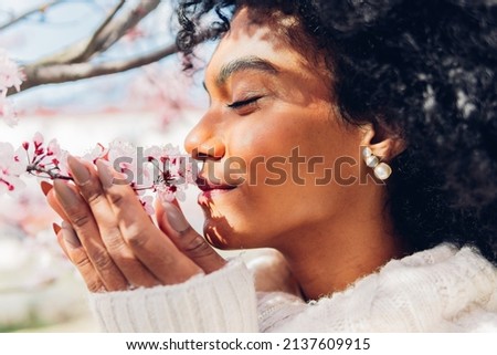 Beautiful African American woman smelling the soft, fresh and natural scent of pink flowers in spring in bloom. Concept of softness, delicacy, purity, femininity, dream of relaxation.