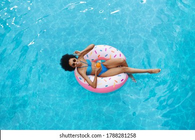 Beautiful African American Woman With Summer Drink Relaxing On Inflatable Ring At Swimming Pool, Overhead View