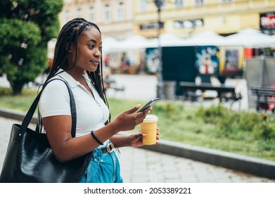 Beautiful african american woman using smartphone and drinking coffee takeaway while out in city