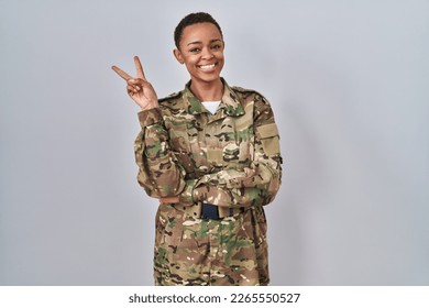 Beautiful african american woman wearing camouflage army uniform smiling with happy face winking at the camera doing victory sign with fingers. number two.  - Powered by Shutterstock