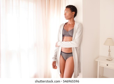 Beautiful African American Woman Wearing Robe And Lingerie In Bedroom With Light Filtering Through Curtains, Home Interior. Health And Intimacy, Beauty Lifestyle, Moody Indoors. Body Silhouette.