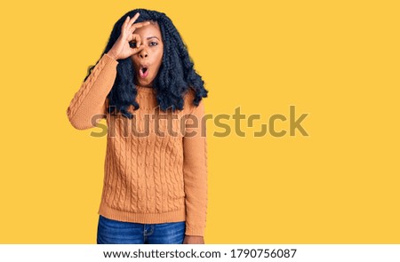 Beautiful african american woman wearing casual  sweater doing ok gesture shocked with surprised face, eye looking through fingers. unbelieving expression. 