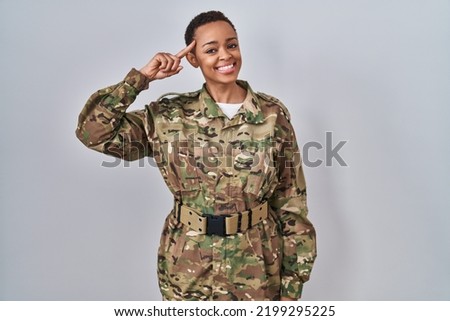 Beautiful african american woman wearing camouflage army uniform smiling pointing to head with one finger, great idea or thought, good memory 