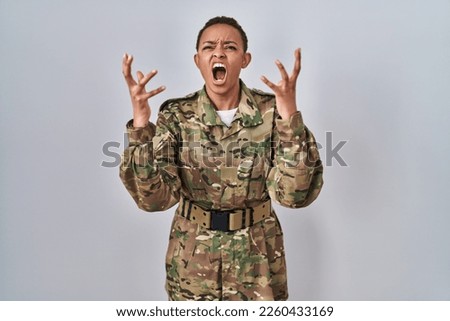 Beautiful african american woman wearing camouflage army uniform crazy and mad shouting and yelling with aggressive expression and arms raised. frustration concept. 