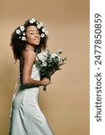 A beautiful African American woman in a white dress, adorned with flowers, holds a bouquet, smiling radiantly against a beige background.