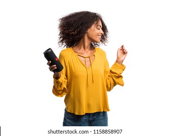Beautiful African American Woman In Yellow Top Enjoying And Dancing At White Background. Modern Trendy Girl With Afro Hairstyle Listening To Music By Wireless Portable Speaker