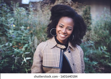 Beautiful african american young woman with afro and large hoop earrings in a stylish coat in a spring park, smiling