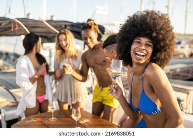 Beautiful african american young woman smiling and dancing looking at the camera, group of friends relaxing on luxury yacht and drinking champagne, having fun together on boat deck at harbour - Powered by Shutterstock