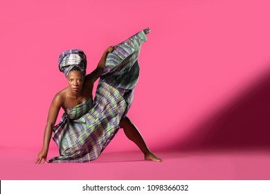 Beautiful African Black Girl Wearing Traditional Colorful African Outfit Does A Dramatic Dance Move Against A Colorful Pink Background