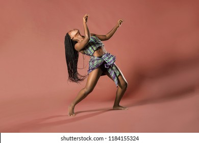 Beautiful African Black Girl Wearing Traditional Colorful African Outfit Does A Dramatic Dance Move Against A Brown Background