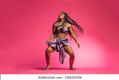 Beautiful African Black Girl Wearing Traditional Colorful African Outfit Does A Dramatic Dance Move Against A Colorful Pink Background