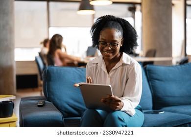 Beautiful African businesswoman sitting on sofa in office. Young woman using digital tablet. 
