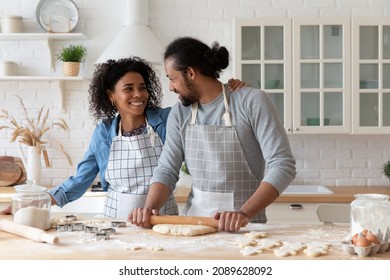 Beautiful African Couple In Love Cooking Together In Modern Kitchen, Husband Holds Rolling-pin Flattening Dough, Young Spouses Preparing Biscuits For Family Holiday Enjoy Cookery At New Own First Home