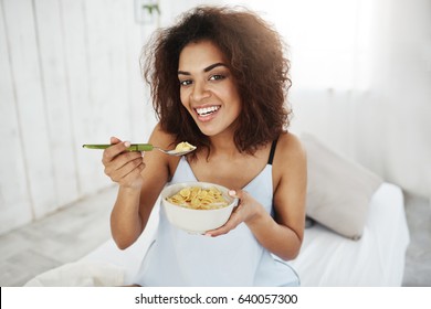 Beautiful african girl in sleepwear smiling looking at camera eating flakes with milk at home in the morning. Copy space. - Shutterstock ID 640057300