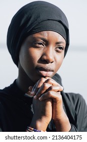 Beautiful African girl with a thoughtful expression and frown clasping her hands in a silent prayer; Adolescent uncertainty and fear of the future