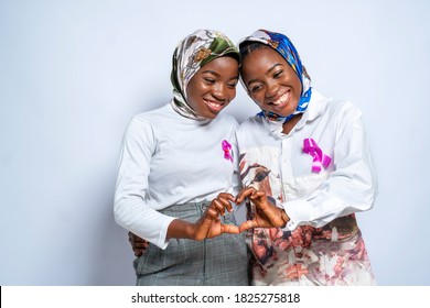 Beautiful African identical Muslim twins wearing hijab with pink ribbon on dress,forming love sign with hand-concept on black millennials and cancer awareness - Shutterstock ID 1825275818