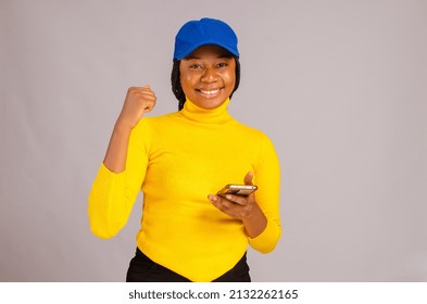 Beautiful African Lady Isolated Over White Background Wearing Yellow Top Excited About What She Saw On Her Phone